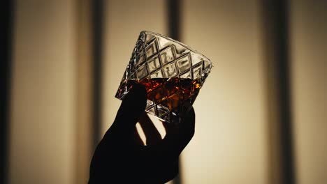 Zeitlupenaufnahme-Einer-Hand,-Die-Ein-Glas-Bourbon-Whisky-Im-Gegenlicht-Schwenkt