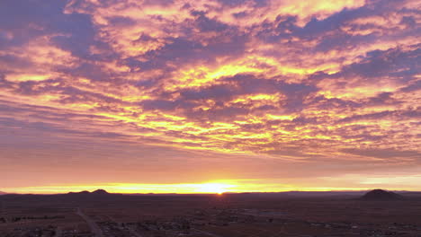 Mojave-desert-at-sunrise-with-vivid-orange-and-purple-clouds,-aerial-view,-timelapse