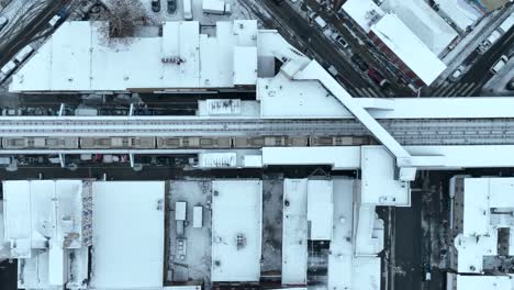 Top-down-aerial-tracking-shot-of-passenger-commuter-train-in-snowy-American-city