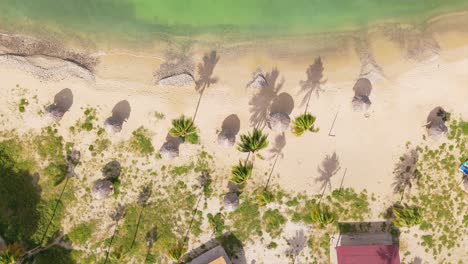 Tropical-beach-bungalow-umbrellas-and-calm-ocean-waters-on-white-sand,-aerial-static