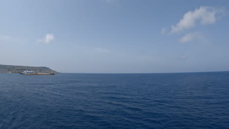 Sailing-on-calm-Mediterranean-sea-with-a-clear-sky-ahead,-Mgaar-port-on-the-horizon