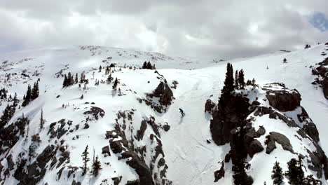 Backcountry-powder-snowboarder-Colorado-Rocky-Mountains-ride-down-couloir-spring-slush-fresh-snow-powder-aerial-cinematic-drone-partially-cloudy-weather-Keystone-Montezuma-Deer-Creek-backwards-motion