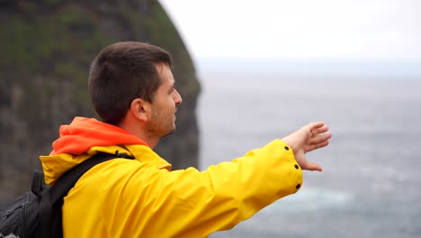 Man-in-yellow-jacket-pointing-and-explaining-what-he-sees-with-hand-movements-Faial,-Azores