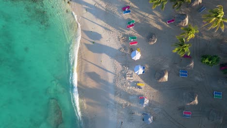 Aerial-static-view-of-crystal-clear-water-in-Curacao-and-multicolored-chairs-with-palm-tree-shadows