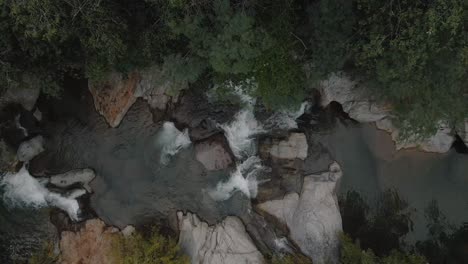 Aerial-view-above-a-beautiful-river-stream-with-rocks-inside-a-wild-forest