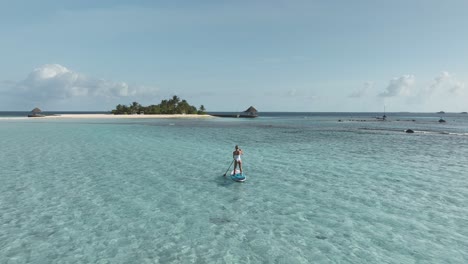 Fit-woman-on-standup-paddleboard-rowing-towards-tropical-island-in-Maldives