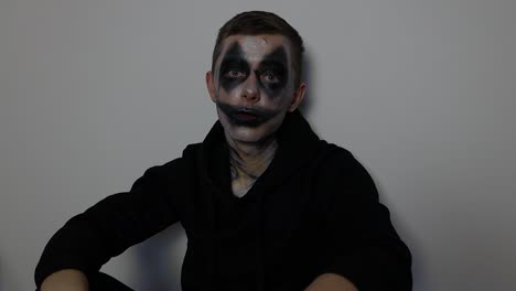 Young-Caucasian-man-with-black-clown-Halloween-makeup-sitting-down-and-talking-to-the-camera