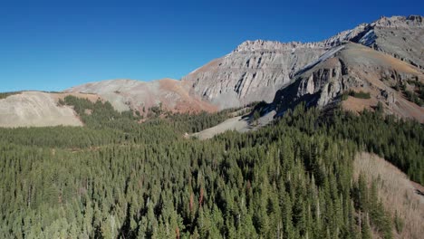 Cinematic-drone-shot-panning-across-a-pine-tree-forest-and-rocky-mountain-peaks