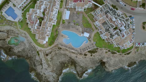 A-high-altitude-aerial-captures-the-Mallorca,-Spain-coastline,-showcasing-the-rooftops-of-tourist-accommodation,-and-outdoor-swimming-pools,-and-embodying-the-concepts-of-travel-and-vacation