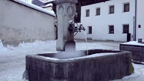 The-village-fountain-in-winter-with-running-water-and-some-light-snow-cover-in-the-town-center-of-Innichen---San-Candido,-South-Tyrol,-Italy