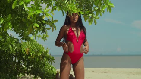 Dressed-in-a-red-bikini,-an-Indian-girl-adds-charm-to-a-Caribbean-tropical-beach-scene-kneel-in-the-sand