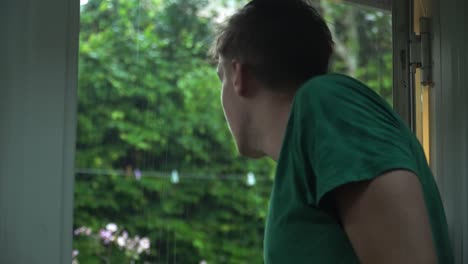 White-Man-in-Green-T-Shirt-Looking-out-of-Door-to-Rainy-Garden