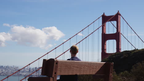 San-Francisco,-Kalifornien-–-Ein-Junger-Mann-Sitzt-Auf-Einer-Bank-In-Unmittelbarer-Nähe-Der-Golden-Gate-Bridge-–-Mittlere-Aufnahme