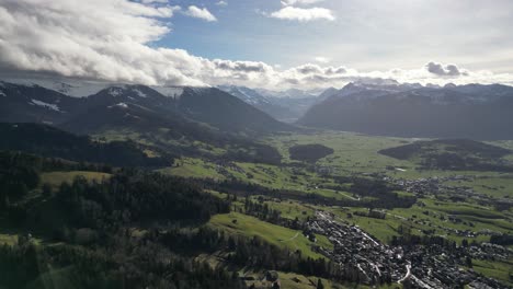 Wunderschöne-Filmische,-Kreisende-Drohnenaufnahme-Von-Wolkenverhangenen-Berggipfeln-Und-Einem-Dorf-Darunter,-Schweiz,-Tagsüber