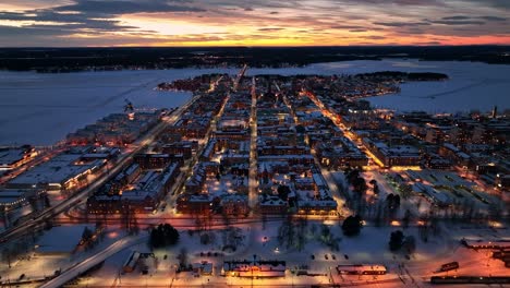 Luleå-city-at-dusk-with-street-lights-and-snow-covered-landscape,-aerial,-aerial-view