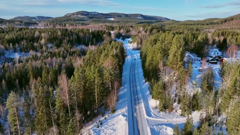 A-snowy-landscape-with-a-road-in-skorped,-sweden,-surrounded-by-coniferous-forest,-aerial-view