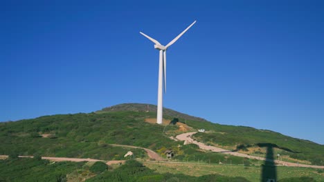 Wind-turbine-on-top-of-a-hill-with-a-clear-blue-sky-in-the-background