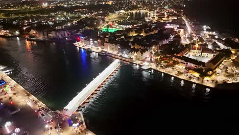 Pontoon-bridge-of-Handelskade-Willemstad-Curacao-shines-bright-in-the-evening,-aerial