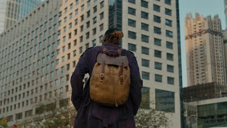 Black-man-exploring-big-city-with-backpack,-view-from-behind