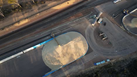 Grain-conveyor-truck-pouring-its-contents-in-an-open-storage-facility,-aerial-top-down