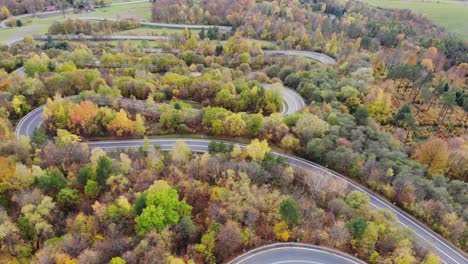 Cars-drive-curvy-scenic-road-in-Wujskie,-Poland-on-sunny-autumn-day,-aerial-view