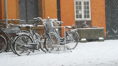 Snowing-in-city,-snowflakes-falling-on-standing-bikes-in-Copenhagen