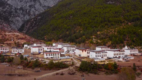Pan-across-uniform-Tibetan-traditional-village-homes-at-base-of-forest-clearing,-Yading-valley