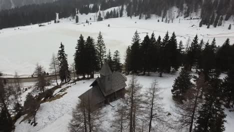 vertigo-drone-of-old-stone-and-wood-church-in-winter-forest-showing-frozen-lake-behind-it