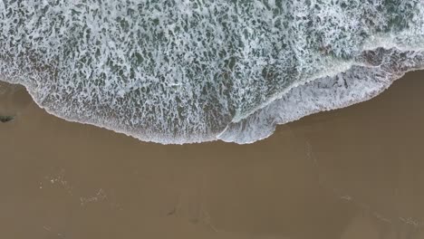 Wet-Sandy-Beach-And-Foamy-Rolling-Ocean-Waves---Aerial-Top