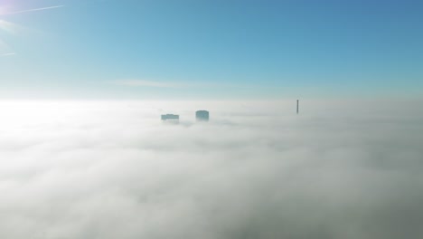 Sunlit-aerial-winter-cloud-journey:-Drone-moves-forward-towards-towering-skyscrapers-piercing-through-inversion-clouds-revealing-city-views