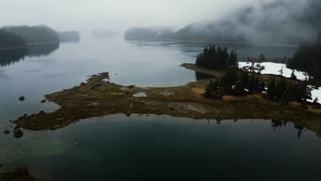 Aerial-view-tilting-over-wetlands-and-calm-waters-of-foggy-Granite-bay,-Alaska