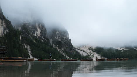 People-preparing-tourism-row-boats-on-Braies-lake-time-lapse-under-misty-Dolomites-mountain-valley