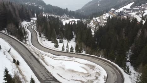 red-car-driving-on-serpentines-twisted-road-snowy-in-mountains-and-skiing-hotel-resort