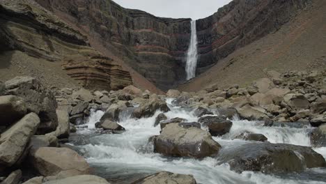 Un-Río-Que-Fluye-Con-Fuerza-Sobre-Rocas-Con-Una-Espectacular-Cascada-Al-Fondo