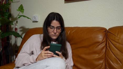 Woman-reading-news-on-mobile-phone-while-sitting-on-brown-couch