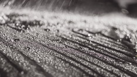 Close-Up-of-Water-Sprayed-and-Rolling-Drops-on-a-Sleek-Black-Surface-in-slow-motion
