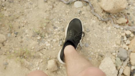 POV-closeup-shot-of-man's-shoes-walking-on-dry-rugged-terrain,-slow-motion