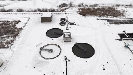 Water-treatment-plant-covered-by-snow,-drone-approach-to-snowy-landscape