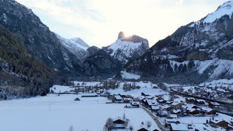 Small-town-below-jagged-alps-mountain-peaks-in-winter-snow-at-dusk