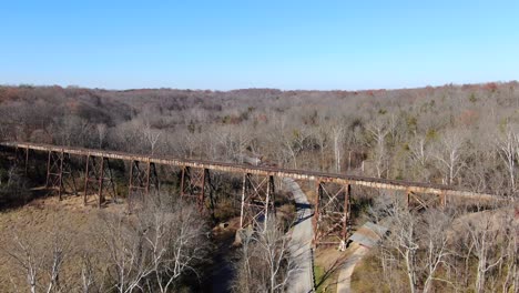 Aerial-Shot-Pushing-Forward-Along-a-Road-Towards-the-Pope-Lick-Railroad-Trestle-in-Louisville-Kentucky,-with-a-Forest-in-the-Background-on-a-Sunny-Day