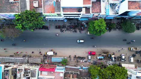 Motorbike-riders-drive-quickly-down-compact-building-lined-street-in-Madurai-India,-aerial-bird's-eye-view