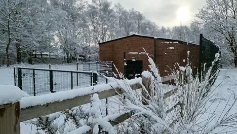 Snowy-brick-farmhouse-storage-barn-surrounded-by-secure-metal-fencing-in-rural-countryside-woodland