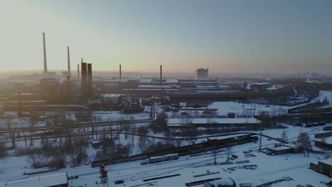 Aerial-view-of-snow-covered-industrial-area,-with-various-buildings-and-structures-under-a-golden-sky-insunrise