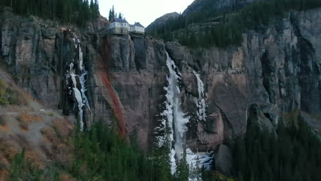 Bridal-Veil-Falls-Telluride-Colorado-aerial-drone-frozen-ice-waterfall-autumn-sunset-cool-shaded-Rocky-Mountains-Silverton-Ouray-Millon-Dollar-Highway-historic-town-landscape-slow-right-pan-up-reveal