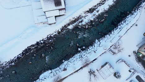 Rocky-river-stream-flowing-through-small-Swiss-town-in-winter-snow