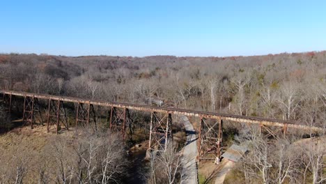 Aerial-Shot-Pushing-Forward-Along-a-Road-Towards-the-Pope-Lick-Railroad-Trestle-in-Louisville-Kentucky,-with-a-Forest-in-the-Background-on-a-Sunny-Day