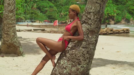 Eine-Tropische-Flucht-Entfaltet-Sich-Mit-Einem-Schwarzen-Mädchen,-Das-Einen-Roten-Bikini-Trägt,-An-Einem-Weißen-Sandstrand-In-Der-Karibik,-Der-Sich-An-Einen-Baum-Lehnt