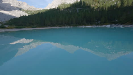 FPV-drone-speeding-across-stunning-blue-alpine-lake-reflecting-Italian-Dolomite-mountains-mirrored-in-waters-surface