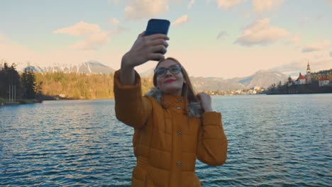 Vídeo-De-4k-De-Una-Hermosa-Joven-Caucásica-Tomando-Una-Foto-Selfie-En-Un-Destino-Turístico-Muy-Famoso-Bled,-Eslovenia