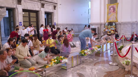 Devout-Buddhist-worshippers-offering-flowers-in-front-of-the-altar-of-a-Buddha-inside-a-temple-in-the-middle-of-Bangkok,-Thailand
